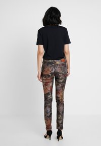 Pantaloni a fantasia floreale in tonalità scure con sfumature di marrone, verde e rosso; vestibilità alta in vita, materiale in cotone e dettaglio in pelle sul retro.