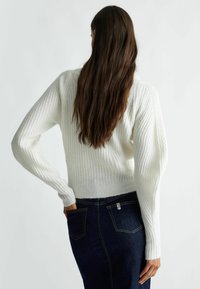 Maglione bianco a coste con maniche lunghe, vita aderente, motivo testurizzato, abbinato a jeans di denim scuro. Tessuto morbido e confortevole.
