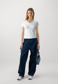 Hvit tettsittende v-hals t-skjorte med rynkede detaljer, kombinert med løse mørkeblå denimbukser og en liten denimveske.