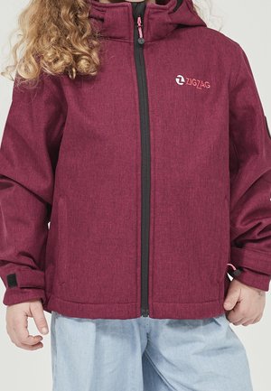 Dziecko ubrane w bordową kurtkę zapinaną na zamek z kapturem oraz jasnoniebieskie spodnie, stojące z rękami swobodnie opuszczonymi wzdłuż ciała.