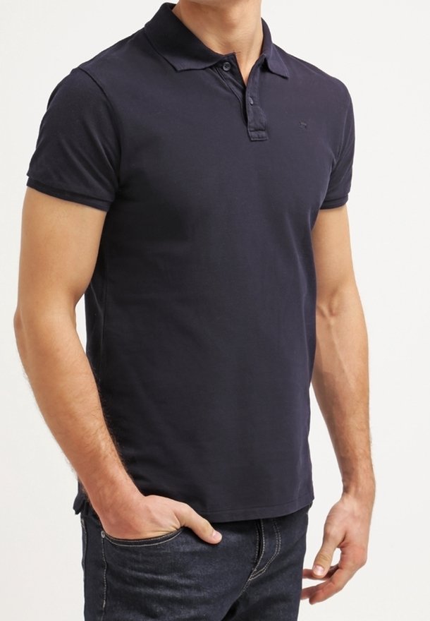Homme portant un polo bleu marine ajusté à manches courtes avec col et patte à deux boutons, associé à un jean bleu foncé.