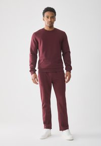 Bordo pulover in skladu z bordo trenirkami iz gladkega materiala, ki ima okroglo ovratnik, rebraste manšete in zožane hlače, v kombinaciji z belimi čevlji.