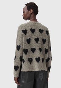 Maglione grigio in lana con una vestibilità comoda, caratterizzato da motivi a cuore nero in rilievo su tutta la superficie. Finitura testurizzata e bordi a costine.