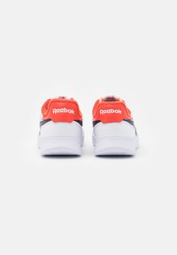 Paire de baskets blanches Reebok avec des accents orange vif au talon et des bandes latérales noires, vues de dos sur un fond blanc.