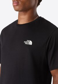 Close-up of a person wearing a black T-shirt with a small white "The North Face" logo on the left chest.