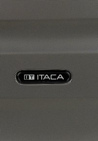 Superficie texturizada negra y plata con una etiqueta rectangular negra que muestra la palabra "ITACA" en letras mayúsculas blancas.