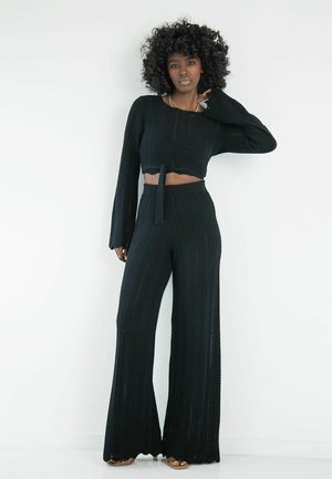 Czarny dzianinowy zestaw składający się z krótkiego topu z długimi rękawami oraz spodni o szerokich nogawkach z teksturowanym wzorem w zygzak.