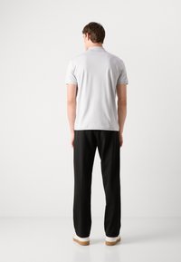 Polo cinza claro com mangas curtas, combinado com calças pretas e sapatilhas brancas com solas de borracha. Design simples e limpo.