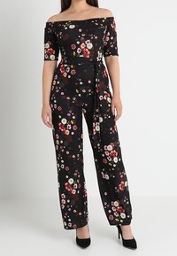 Combinaison noire à fleurs décolletée et à manches courtes, avec une taille ceinturée et un design à jambes larges, ornée d'une variété de fleurs colorées.