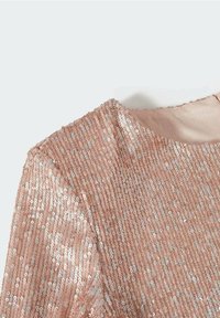 Top en sequins roses avec un tissu texturé et des sequins réfléchissants, décolleté rond et doublure intérieure lisse. Gros plan sur les épaules.