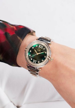 Kuld- ja hõbe käekell rohelise kellapeaga, Roman numbritega XII ja VI, kaunistatud teemantitaoliste aktsentidega ning tekstuuriga kella raami.