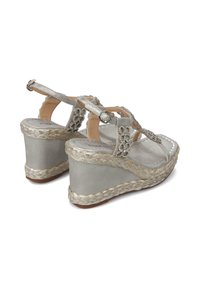 Sandalias de cuña plateadas con suela de yute trenzado, adornos decorativos, correa ajustable en el tobillo y acabado de cuero suave en la parte superior.