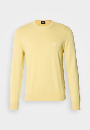 Gul stickad tröja med rund hals och långa ärmar. Har en liten fyrkantig logotyp på bröstet. Slät textur och figurnära design.