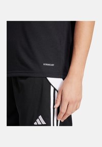 Zwarte sportieve shirt van een gestructureerde stof, met het "AEROREADY"-logo op de zoom. Gecombineerd met zwarte shorts en witte accenten.