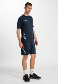 Granatowy zestaw sportowy składający się z koszulki z krótkim rękawem i spodenek z jasnoniebieskimi akcentami w kształcie szewronu, wykonany z lekkiego, oddychającego materiału.