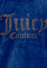 Blå sammetstyg med "Juicy Couture" i gyllene rhinstenar, kännetecknat av en slät textur och en djärv design.