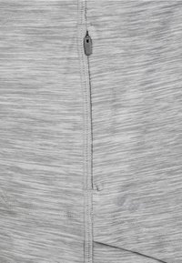 Lichtgrijze sportstof met een gestructureerd patroon, voorzien van een zichtbare rits en versterkte stiksels langs de naad.