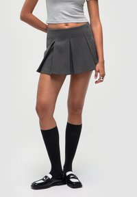Gonna grigia plissettata con vita alta, abbinata a calze nere fino al ginocchio e scarpe nere in pelle lucida con accenti bianchi.