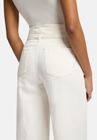 Witte high-waisted broeken hebben twee achterzakken, een gladde textuur en een getailleerd ontwerp, waardoor een gestructureerde silhoutte wordt benadrukt.
