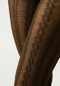 Collant marroni a fantasia con un design testurizzato caratterizzato da un motivo a intreccio e una superficie liscia. La vista ravvicinata mette in evidenza i dettagli.