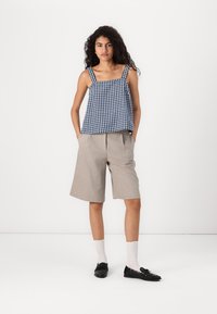 Débardeur à carreaux vichy bleu et blanc avec encolure carrée et bretelles larges, associé à un short gris clair arrivant aux genoux et des mocassins noirs.