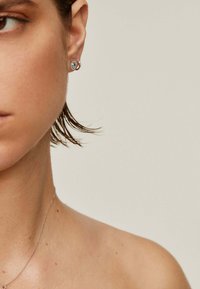 Pendientes de aro de plata con una piedra preciosa azul central, sobre piel neutra, que muestran una textura suave y un diseño minimalista.