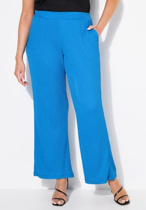 Pantalons larges bleus en tissu texturé, dotés d'une ceinture confortable et de poches latérales. Assortis avec des sandales noires à lanières.