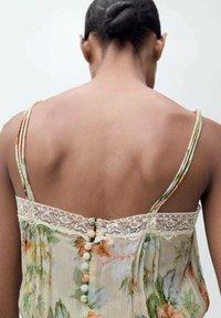 Floral print camisole with lace trim, thin straps, and delicately detailed buttons in pastel colors at the back. Light, flowing fabric.
