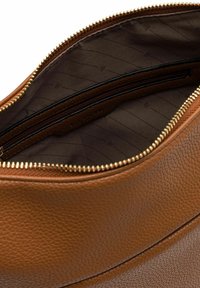 Brown leather handbag interior featuring a gold zipper, smooth lining, and a small zip pocket. The texture is subtly pebbled.