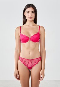 Sujetador de encaje rojo y tanga a juego con bordes festoneados y patrones florales, con detalles transparentes y tirantes finos. Textura suave.