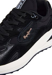 Sneaker nera con texture miste, lacci neri, suola bianca e logo "Pepe Jeans" sul lato vicino al tallone e sulla linguetta.