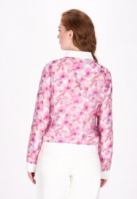 Bloemige bomberjack met een roze en witte aquarelpatroon, geribde manchetten en zoom; lichtgewicht stof, ritssluiting en staande kraag.