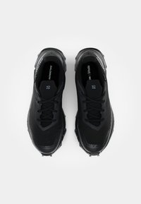 Chaussures de sport noires avec une empeigne en maille texturée, des accents mats et brillants contrastés, et des semelles en caoutchouc épaisses avec un motif de traction.