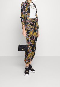 Strój w kwiatowy wzór z czarnym tłem, złotymi akcentami i kolorowymi kwiatami. Dobranie do czarnych sneakersów i czarnej torebki.