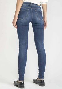 Jean skinny en denim bleu foncé avec taille haute, doté de poches arrière et d'un design lisse et ajusté. Le tissu a une légère texture.
