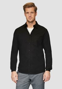 Schwarze, langärmlige Hemdbluse mit einer Tasche auf der linken Seite, aus einem glatten Stoff. Wird über einem weißen Rundhals-T-Shirt getragen.