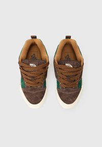 Un paio di sneakers Vans marroni e verdi con lacci marroni spessi e suole in gomma bianca viste dall'alto su uno sfondo bianco.