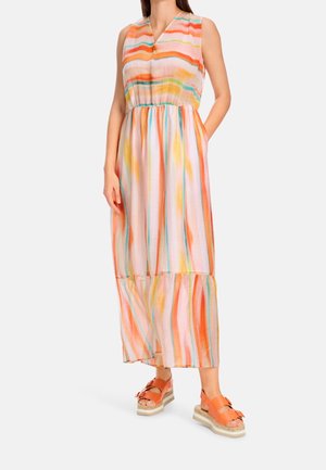 Femme portant une robe maxi sans manches à rayures multicolores avec des poches et des sandales à plateforme orange à semelles épaisses.