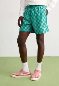 Grønne rutete shorts med elastisk liv og snor, kombinert med rosa sneakers og hvite ankelsokker.