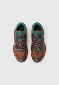 Brune og orange træningssko med meshpaneler, grønne accenter og grå snørebånd. Rund tå og tekstureret sort sål.