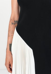 La robe noire et blanche présente un haut noir ajusté et un tissu plissé blanc fluide d'un côté, mettant en avant des textures contrastées.