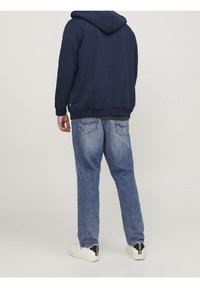 Felpa navy con tasca a marsupio, polsini aderenti e jeans azzurri a vestibilità rilassata con tasche posteriori decorate. Scarpe bianche con dettagli neri.