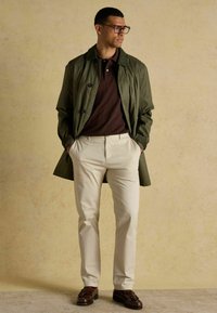 Zaļš viegls mētelis, brūns polo krekls, krēmkrāsas bikses un brūni loaferi. Iespējama pielāgota forma un kontrastējošas tekstūras. Vienkārši dizaina elementi.