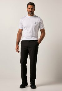 Witte sportieve t-shirt met korte mouwen, textuurstof, zwart logo op de borst, gecombineerd met zwarte broek en zwarte sportschoenen.