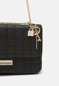 Borsa nera in tessuto con un design trapuntato, tracolla in catena dorata e ciondoli a forma di chiave decorativi. Presenta una placca dorata con il marchio sulla parte anteriore.