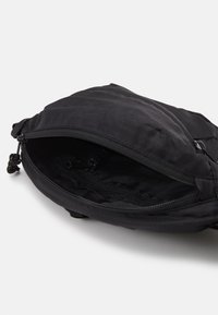 Black fabric bag with a textured surface, top zipper opening, interior pocket, and drawstring hardware. No visible branding or accents.