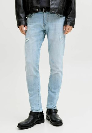 Blugi albaștri deschis, slim fit, cu aspect uzat, purtați cu o curea neagră din piele, cizme negre până la gleznă și o jachetă neagră din piele.