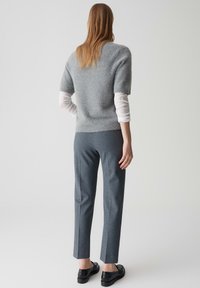 Grijze, fuzzy kortmouwen trui over een witte lange mouwen top, gecombineerd met op maat gemaakte donkergrijze broek en zwarte schoenen.