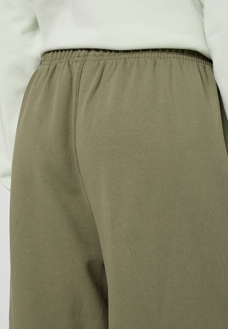 Gros plan sur des pantalons à taille élastique vert olive portés avec un haut clair, montrant la texture du tissu et les détails de couture.
