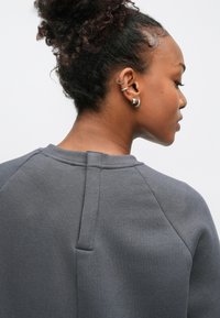 Sweatshirt cinzenta com acabamento texturizado, apresentando um detalhe distintivo de costura nas costas e mangas raglan. Sem quaisquer adornos adicionais.